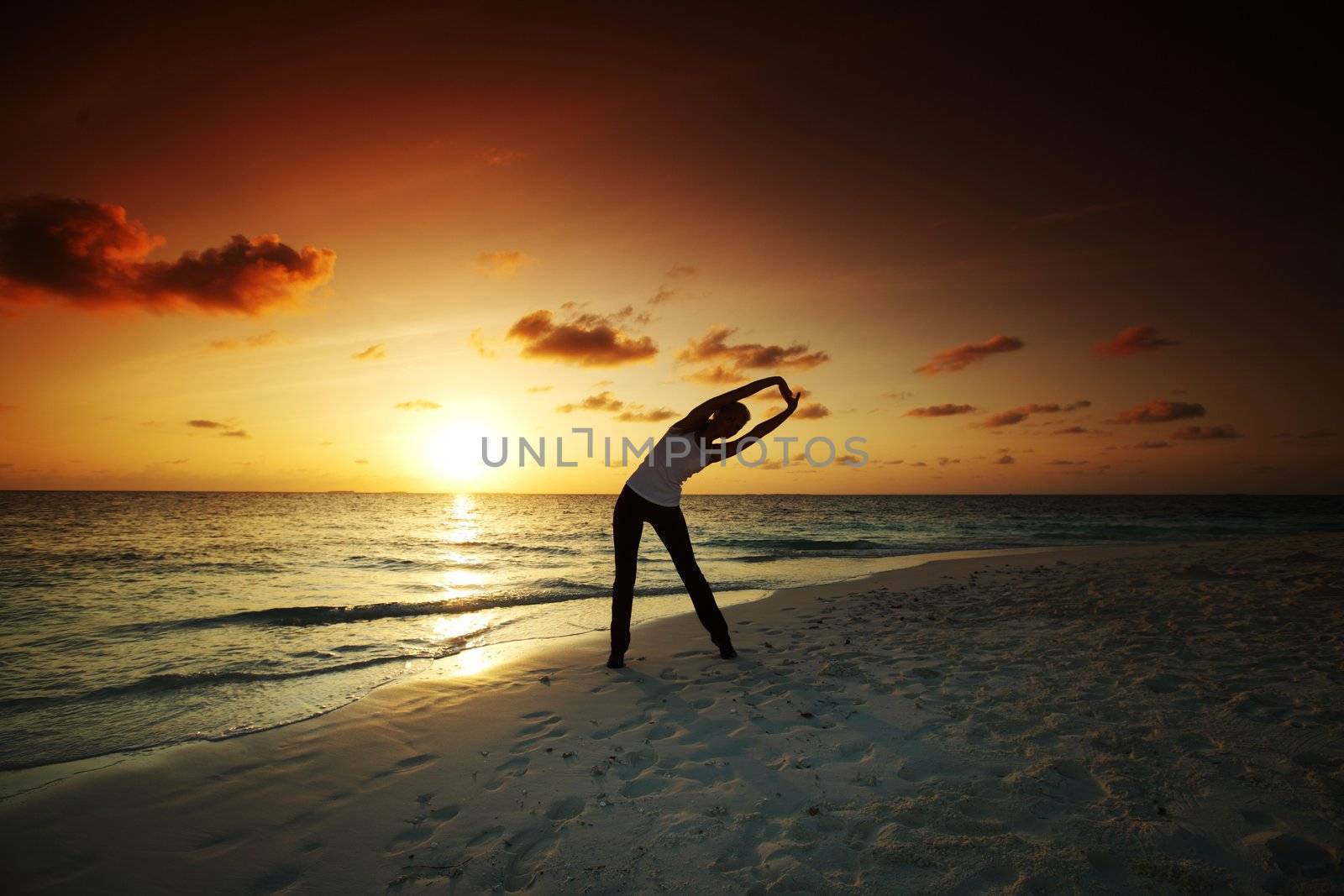 woman practicing yoga the sea coast of sunrise behind