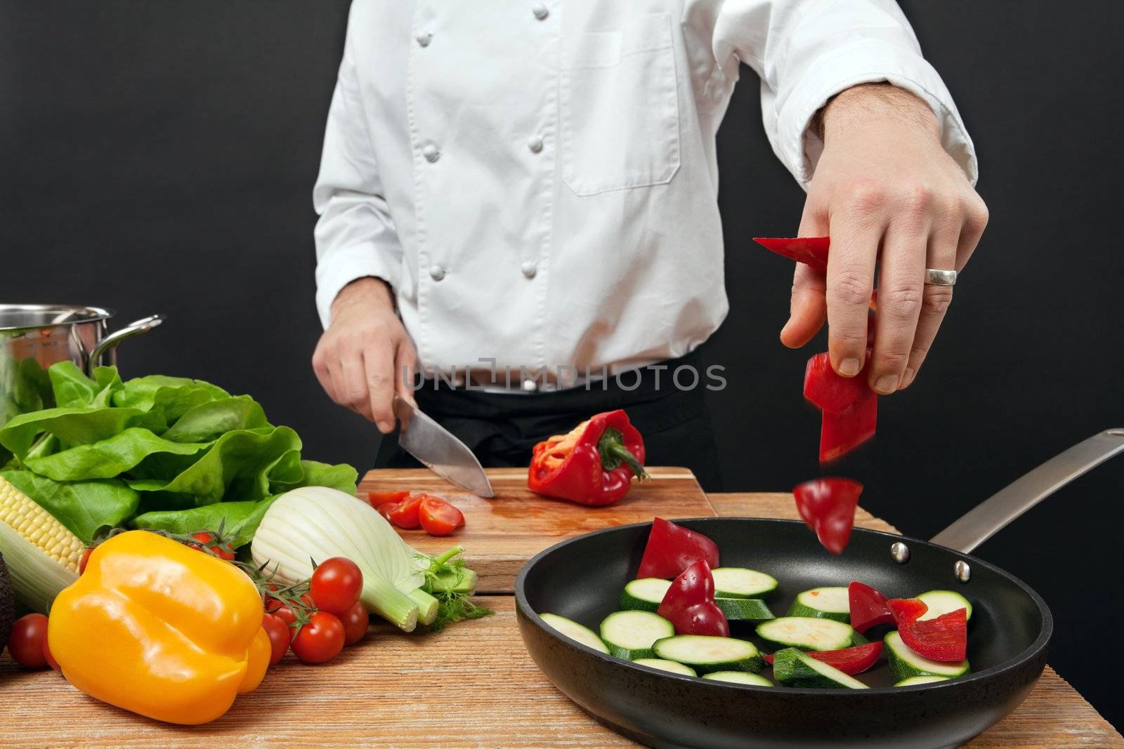Photo of a chef adding chopped vegetables to a pan.