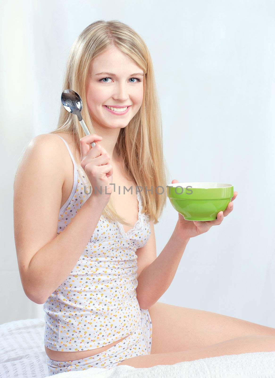 Pretty blond girl sitting on bed and holding spoon and morning meal