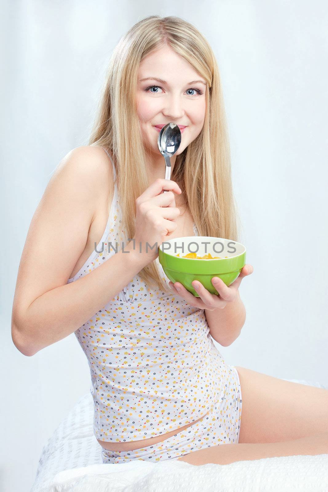 Pretty blond girl sitting on bed and holding morning meal