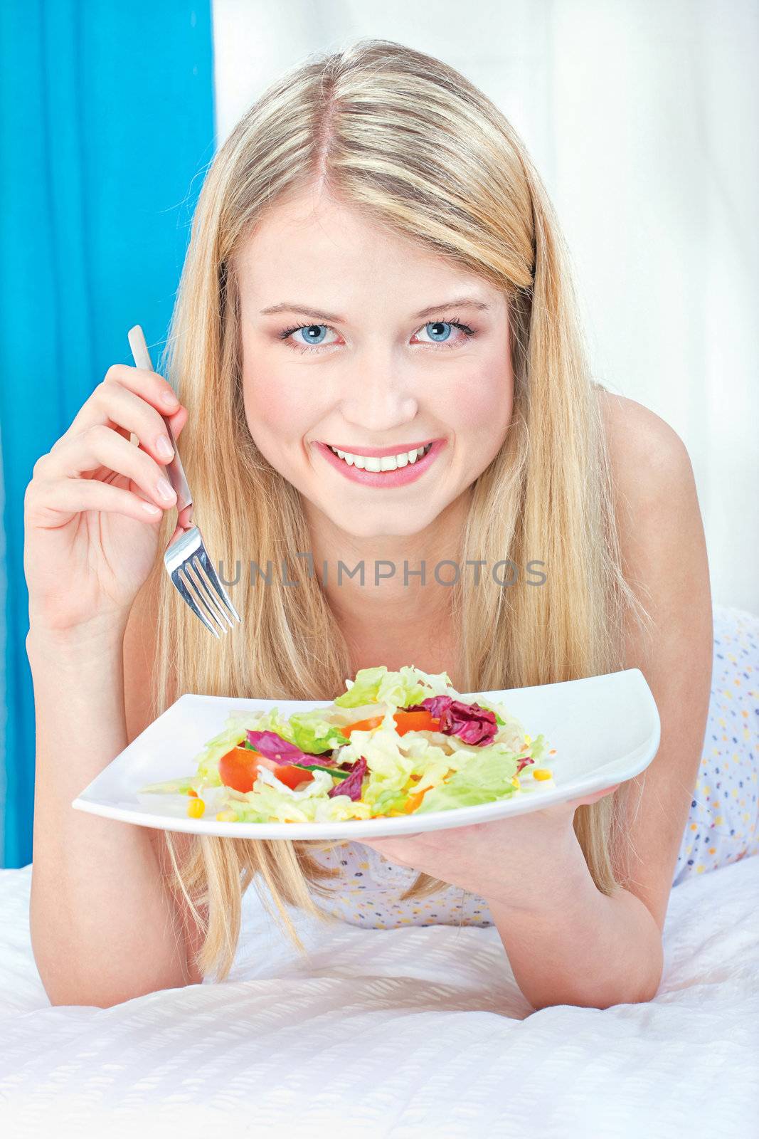 Pretty smiled woman eating salad in bed