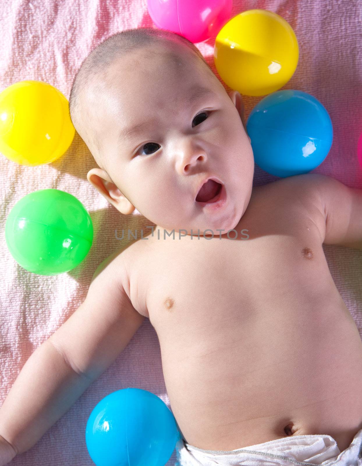 A happy 3 months old baby in a bath of balls.