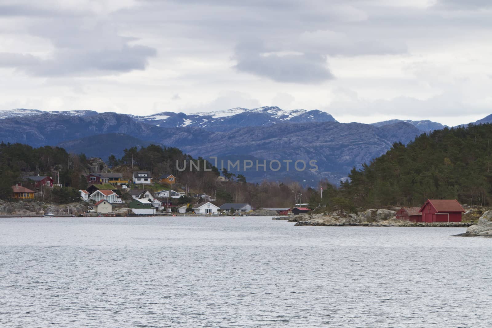 landscape in norway - coastline in fjord with buildings and cloudy sky
