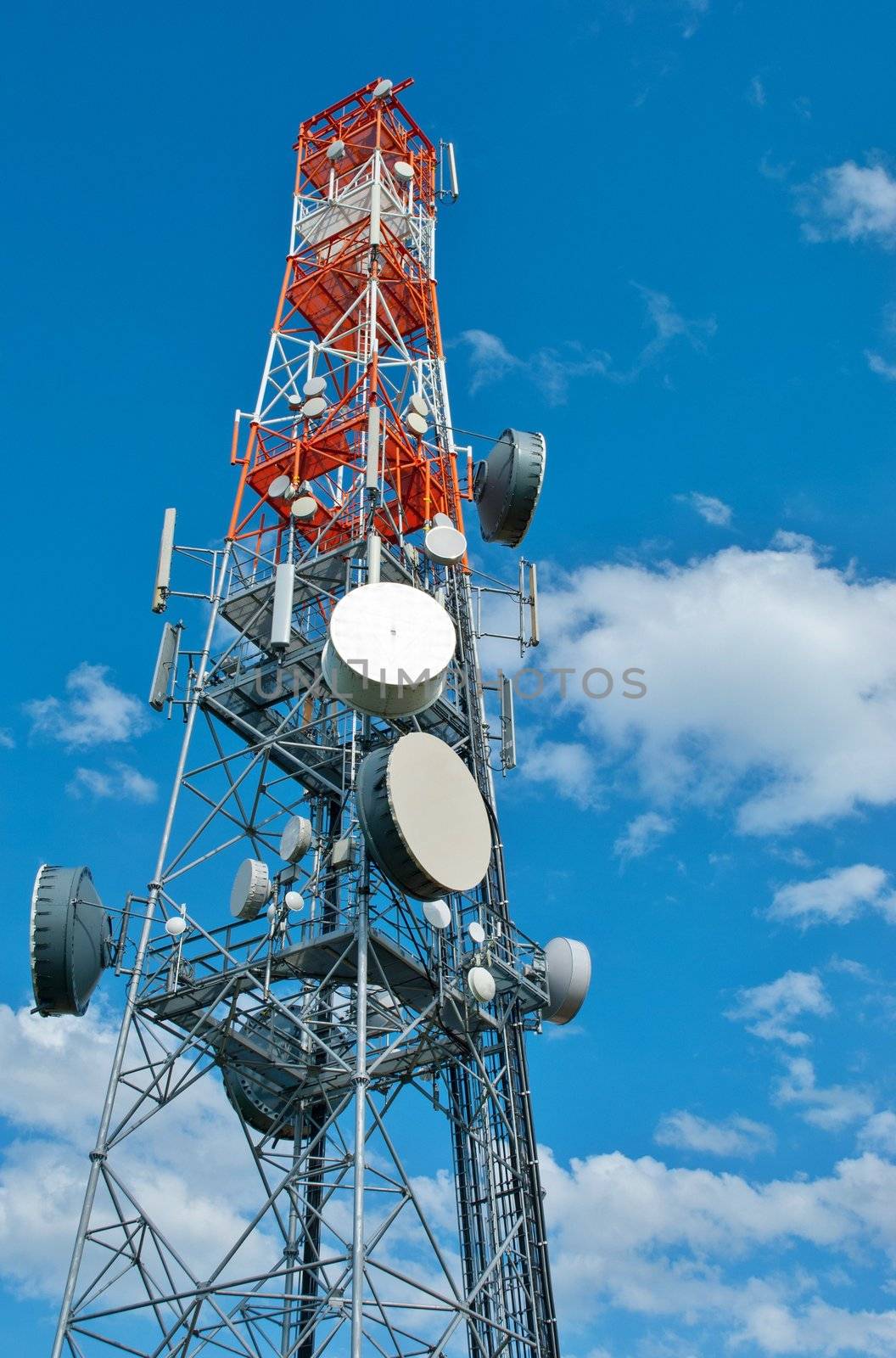 Red and white communication tower with antennas on the blue sky.