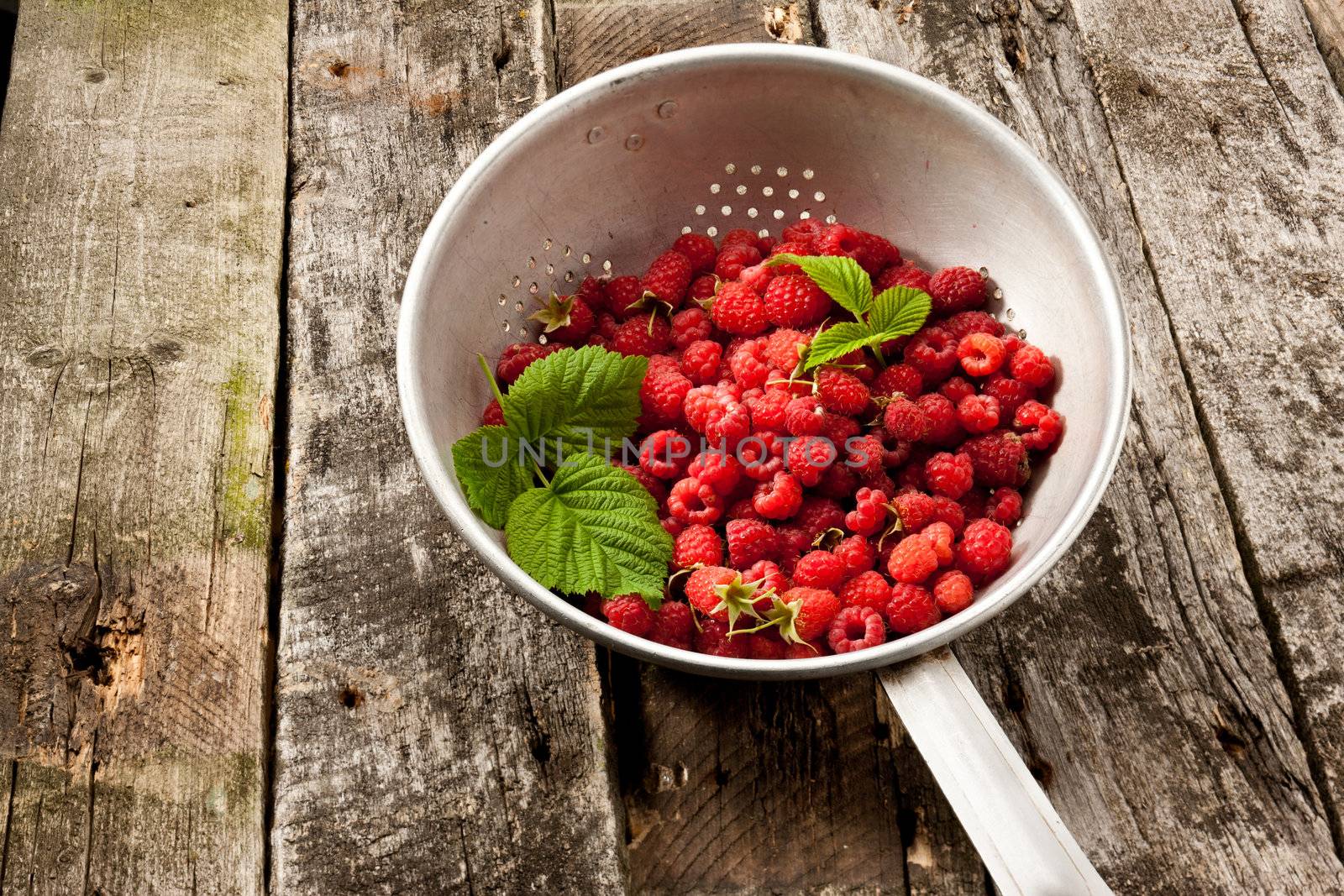 fresh ripe raspberry in collander on wooden table