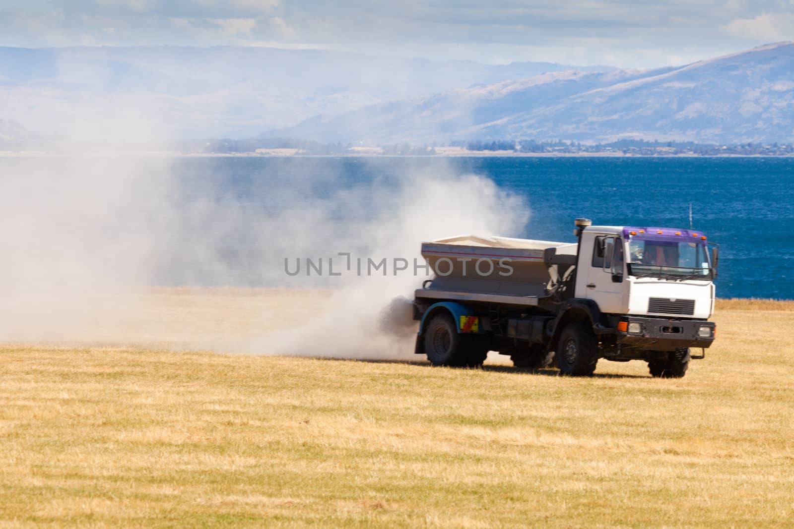 Truck spreading fertilizer on pasture meadow creating an enormous white dust cloud of rock phosphate and potash