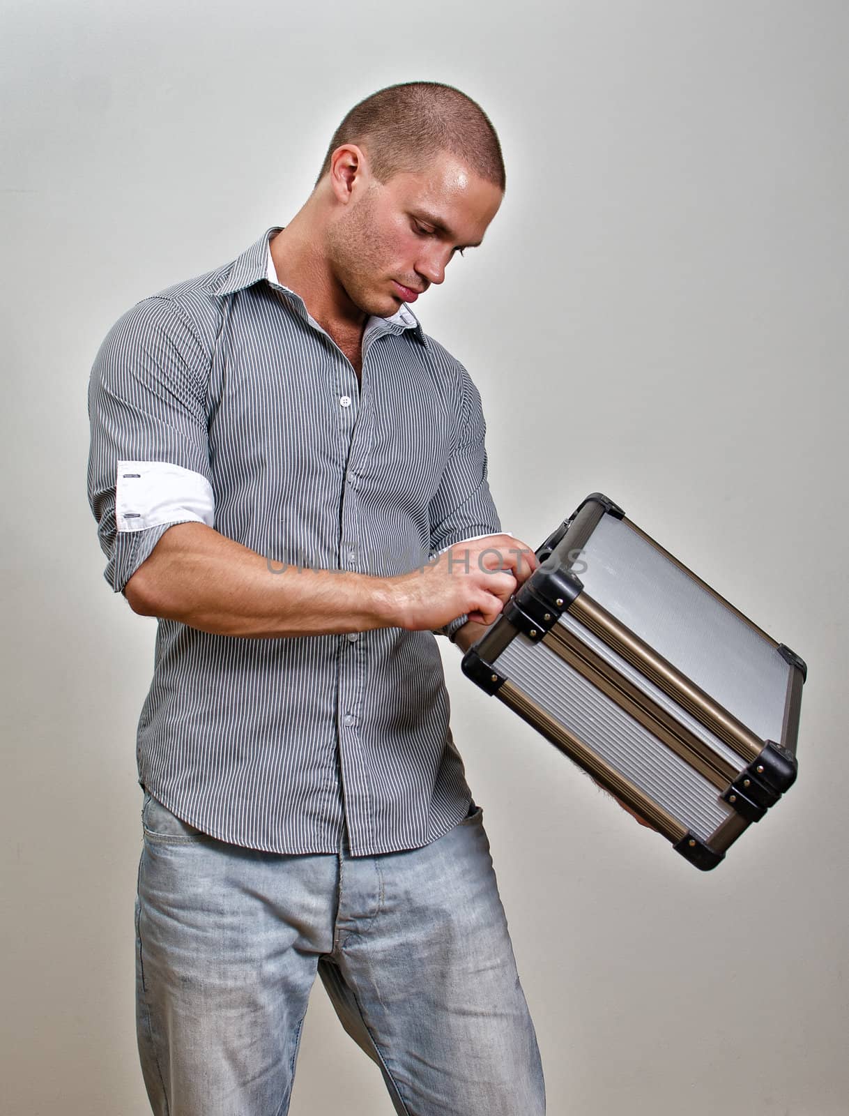 Trendy male holding suitcase. On grey background.