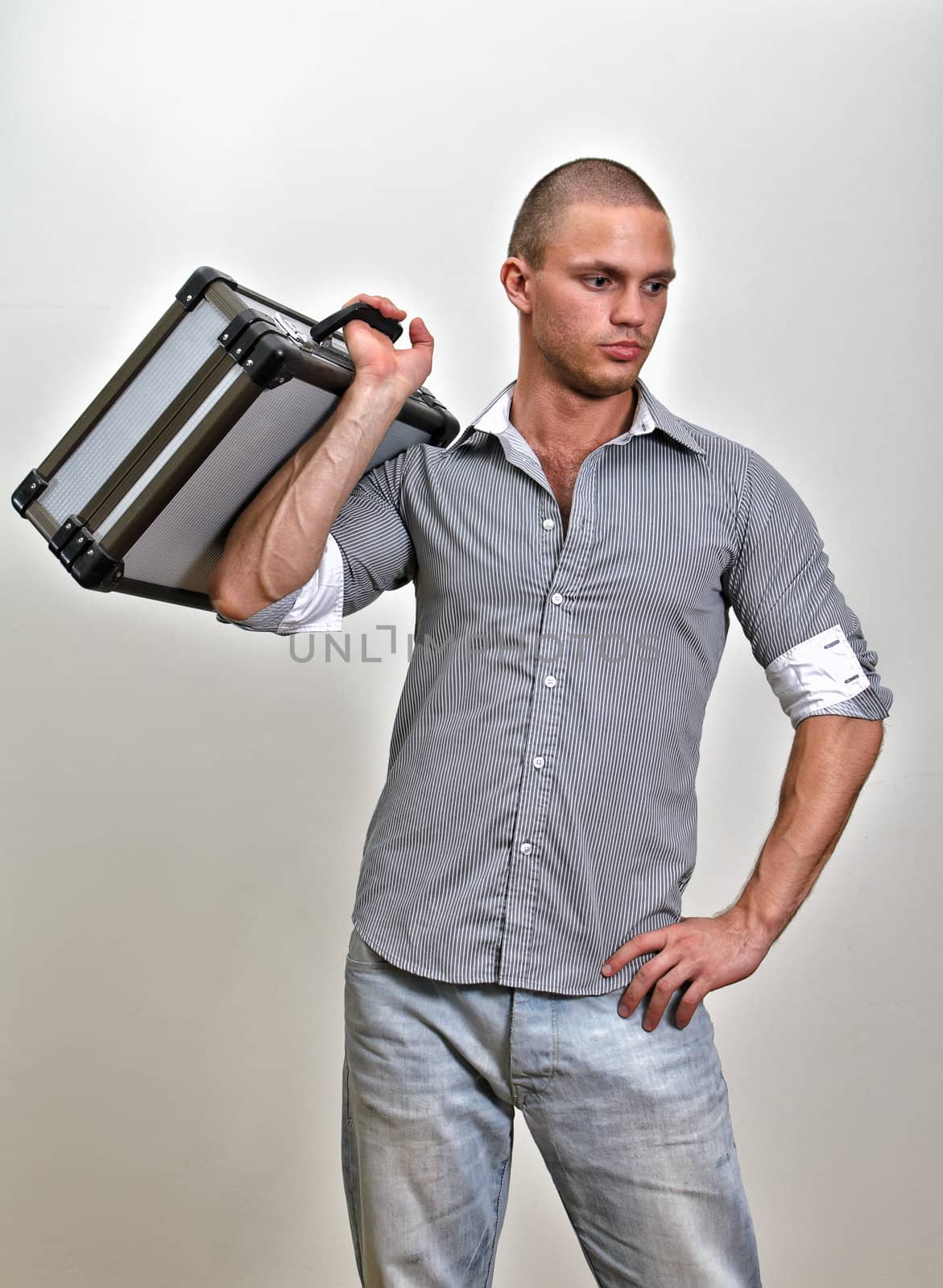 Trendy male holding suitcase. On grey background.