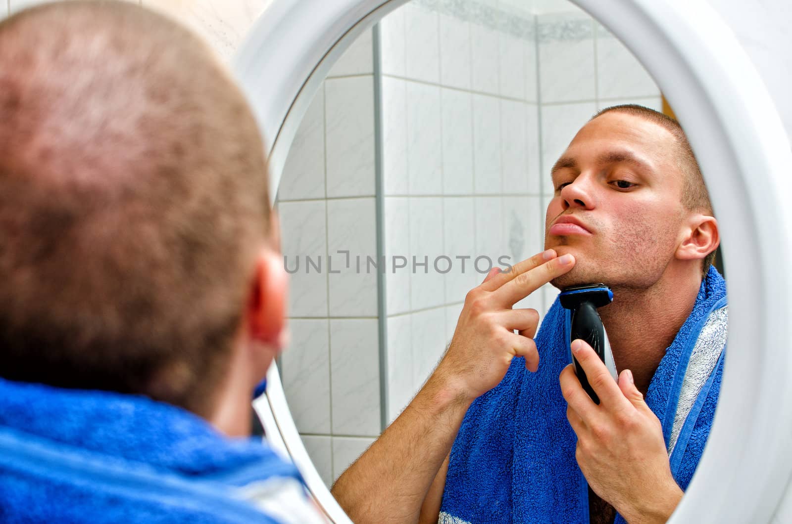 Male with towel shaving in bathroom in front of the mirror. 
