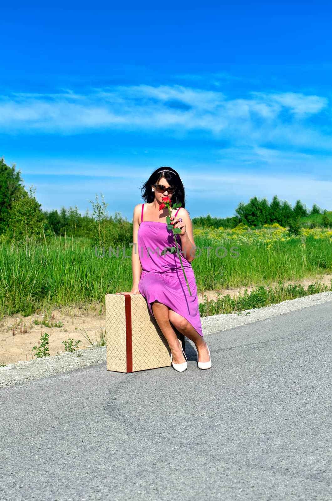 Woman with rose sitting on suitcase on the road.