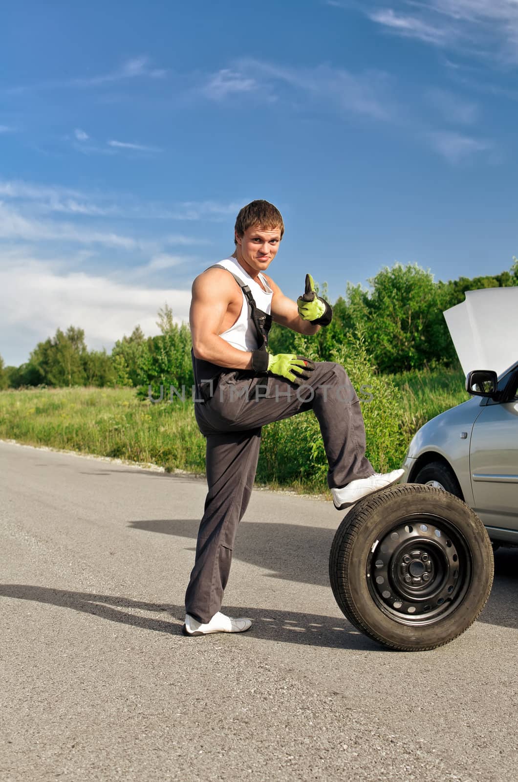 Handsome mechanic with a tire on a road