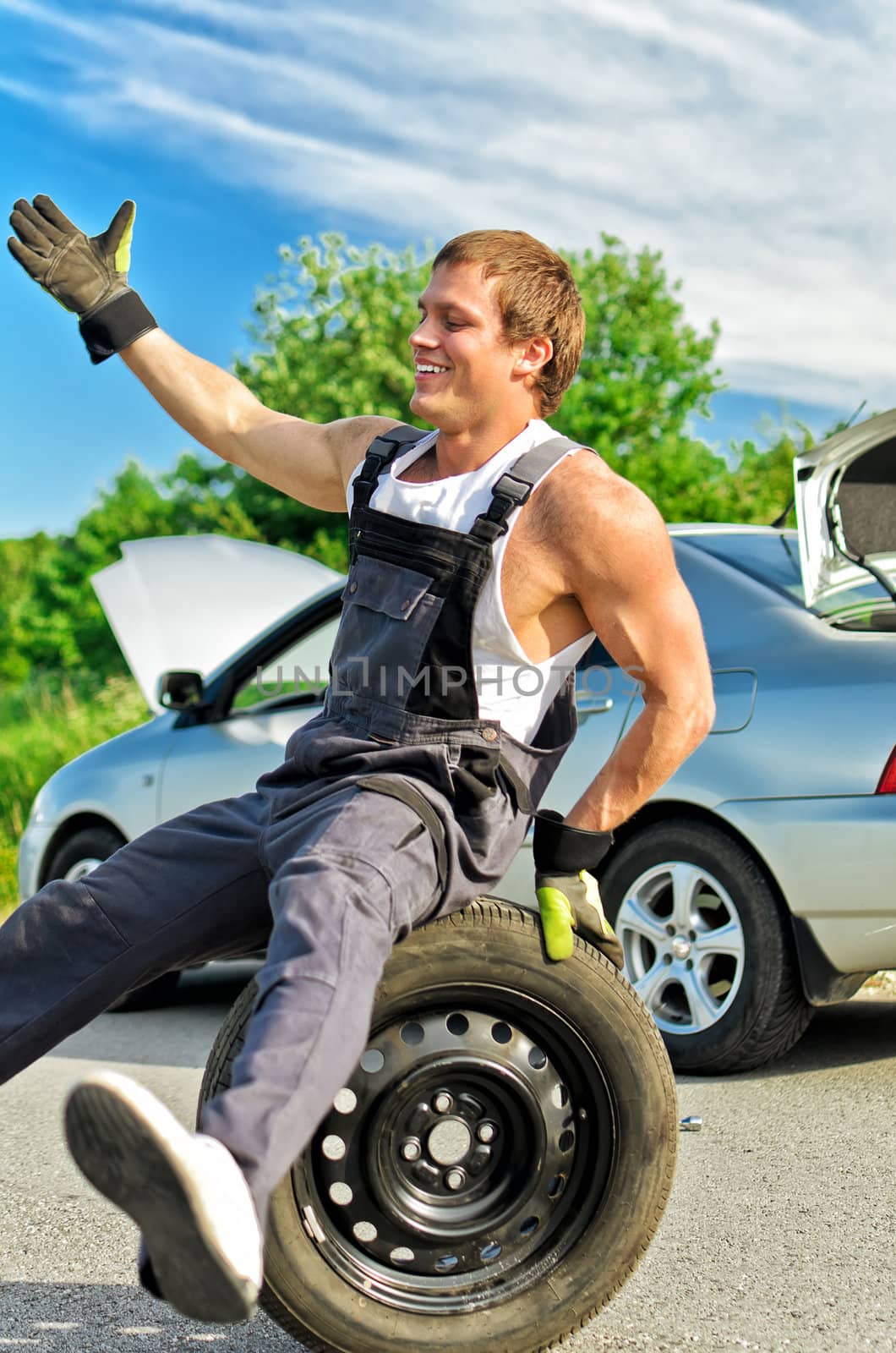 Portrait of laughing mechanic sitting on a tire on a road.