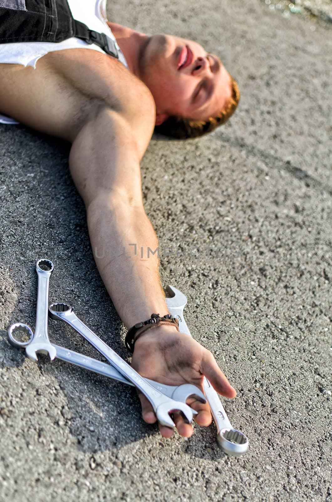Tired mechanic laying on the road with  stainless steel wrench in his hand