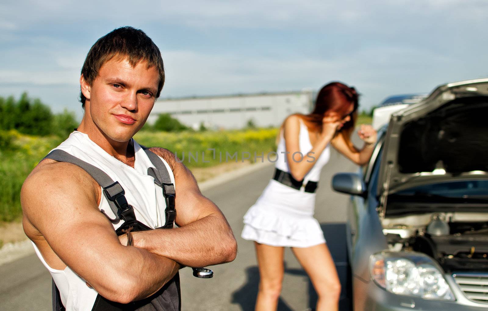 Portrait of a hadsome mechanic with a girl near broken car on a background