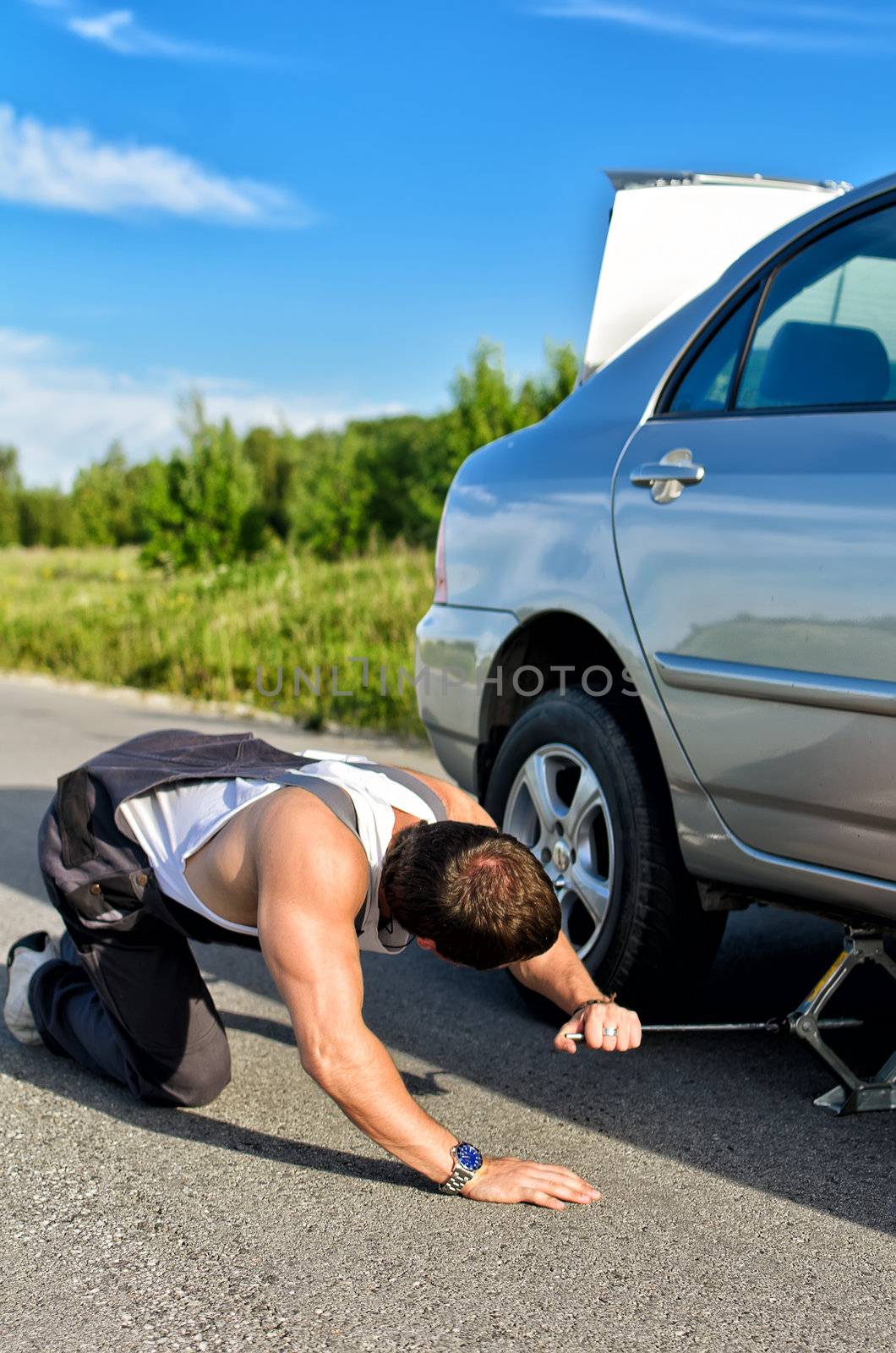 Mechanic sets a jack-screw under the car on a road by dmitrimaruta