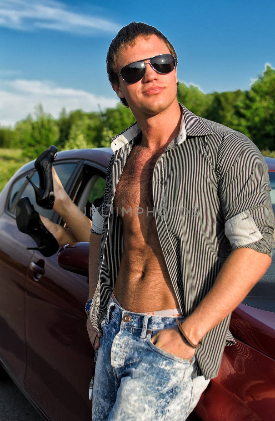 Sexy man posing near the car with woman legs stick out the window