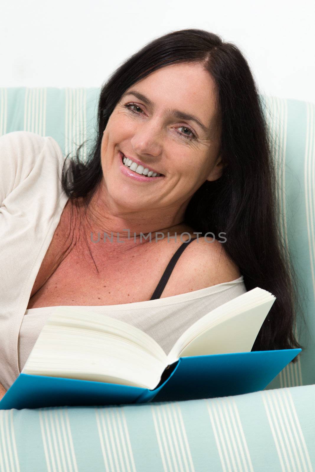 Dark haired woman lying on couch and reading a blue book