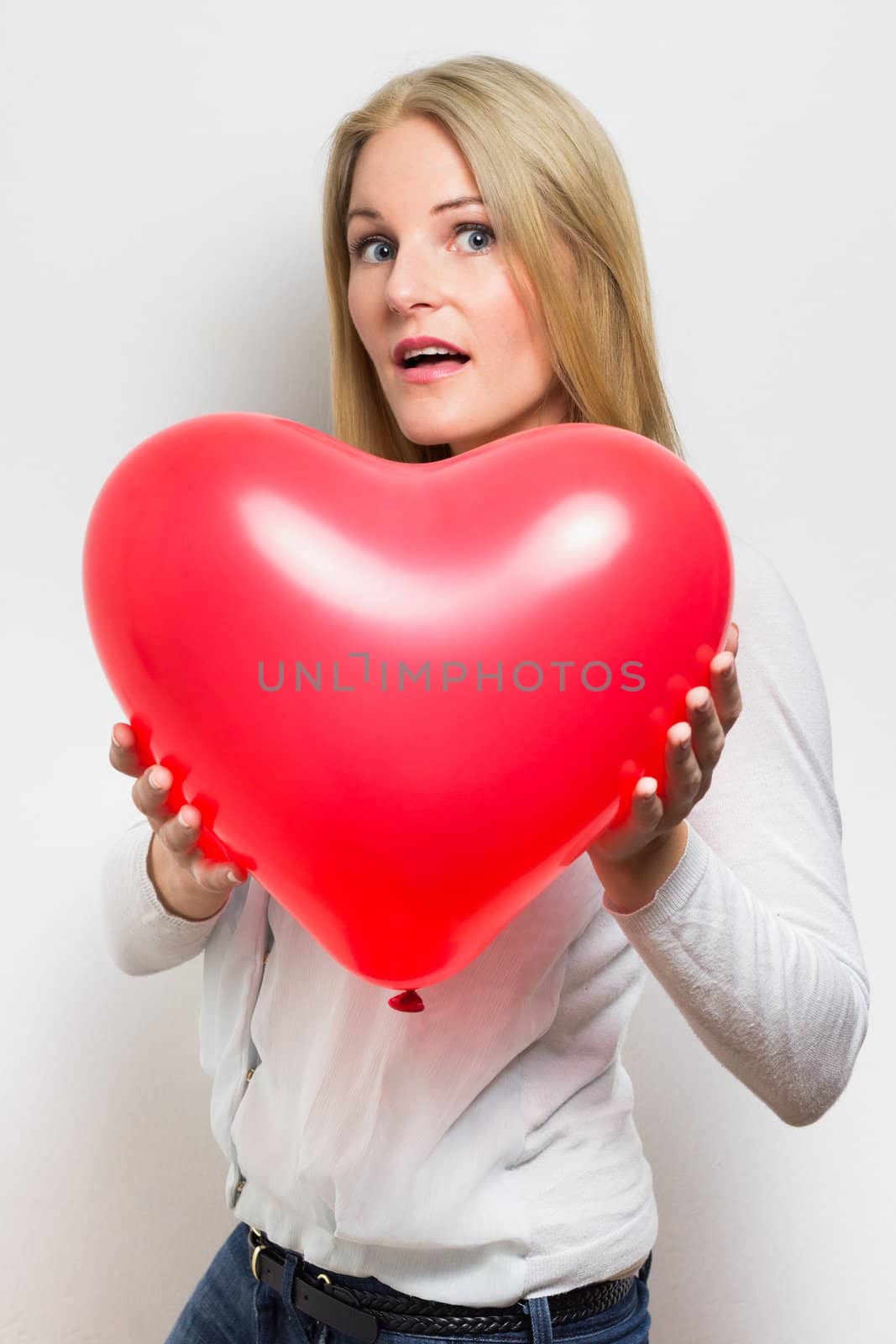 Surprised  caucasian woman holding a red heart balloon