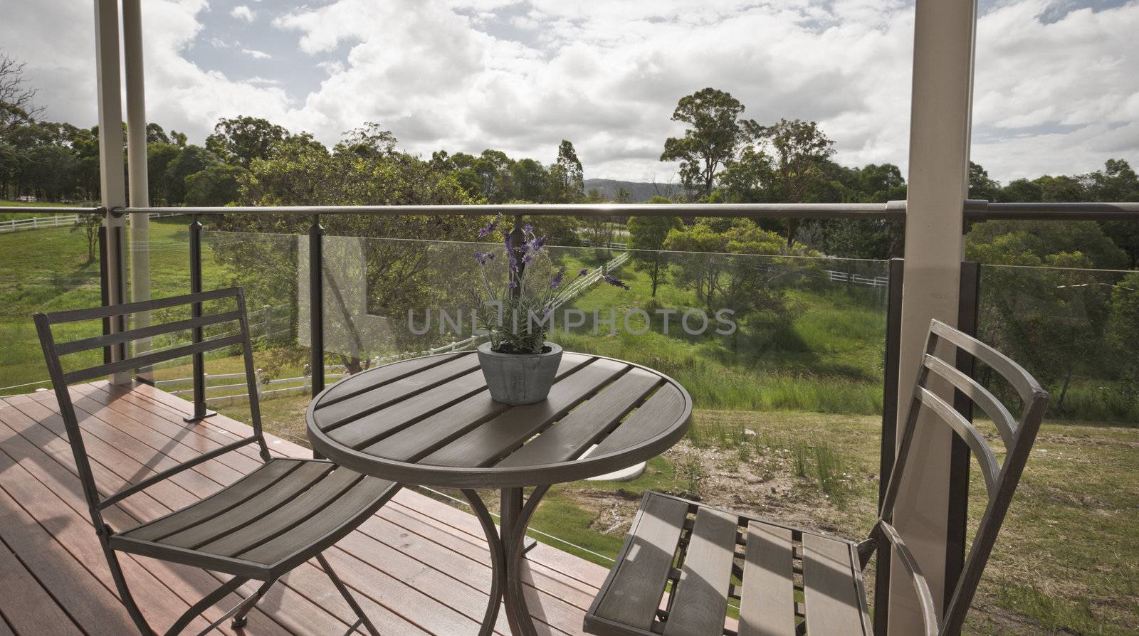 Wooden table and chairs on a glassed in timber deck overlooking green countryside