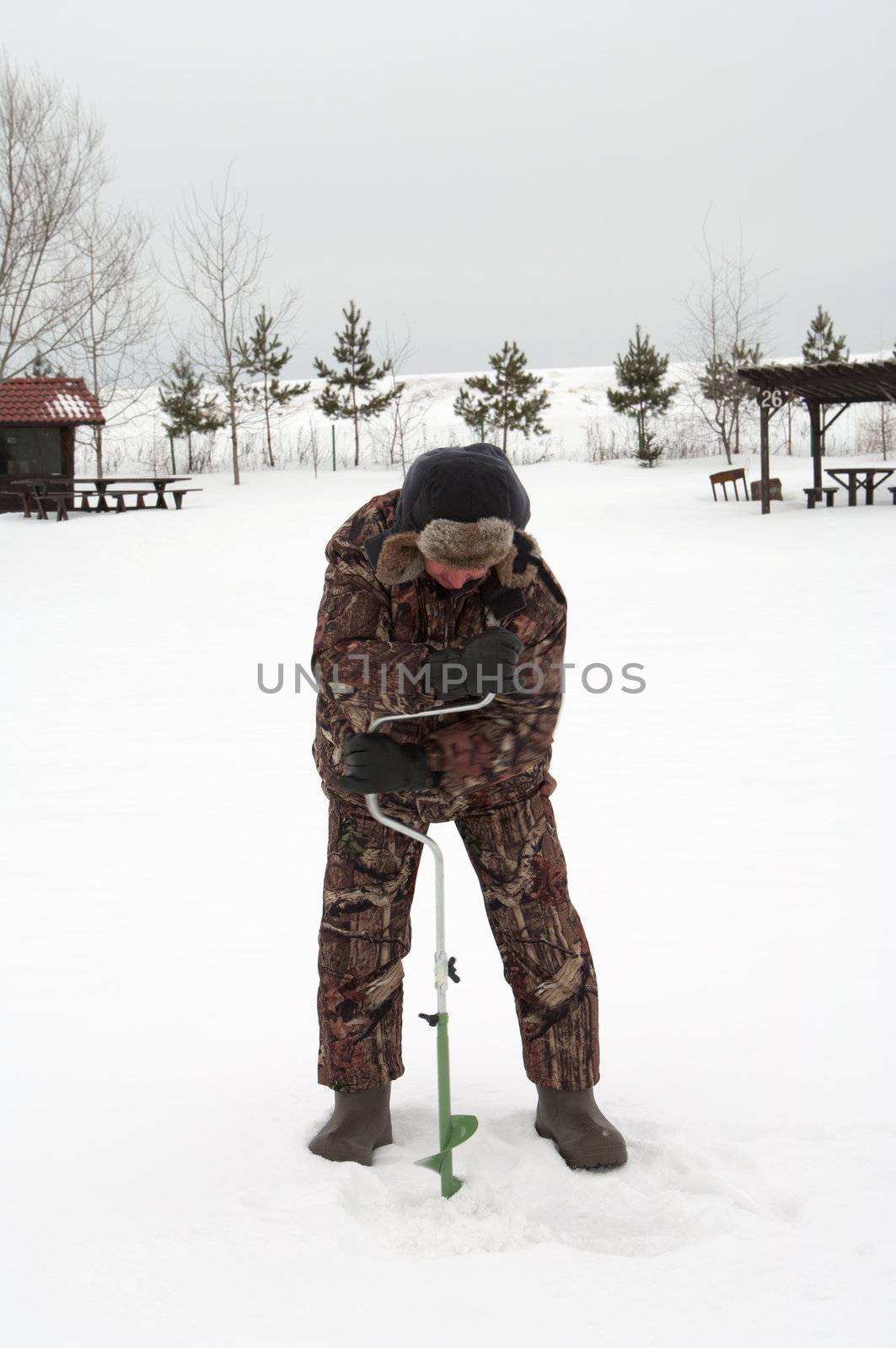 The man drills a hole in lake ice.