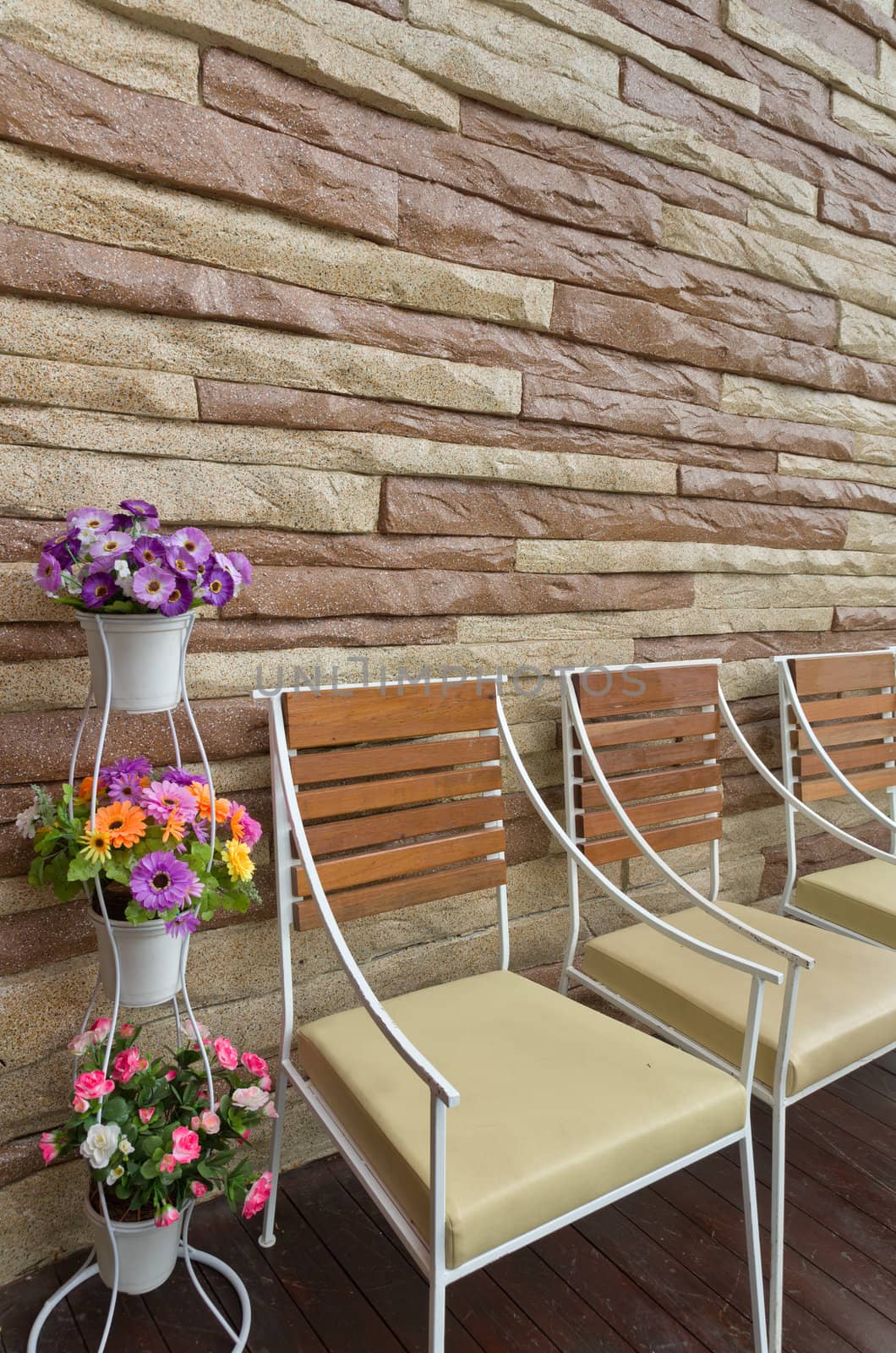 Colorful flowers in white pot wood chair and stone wall