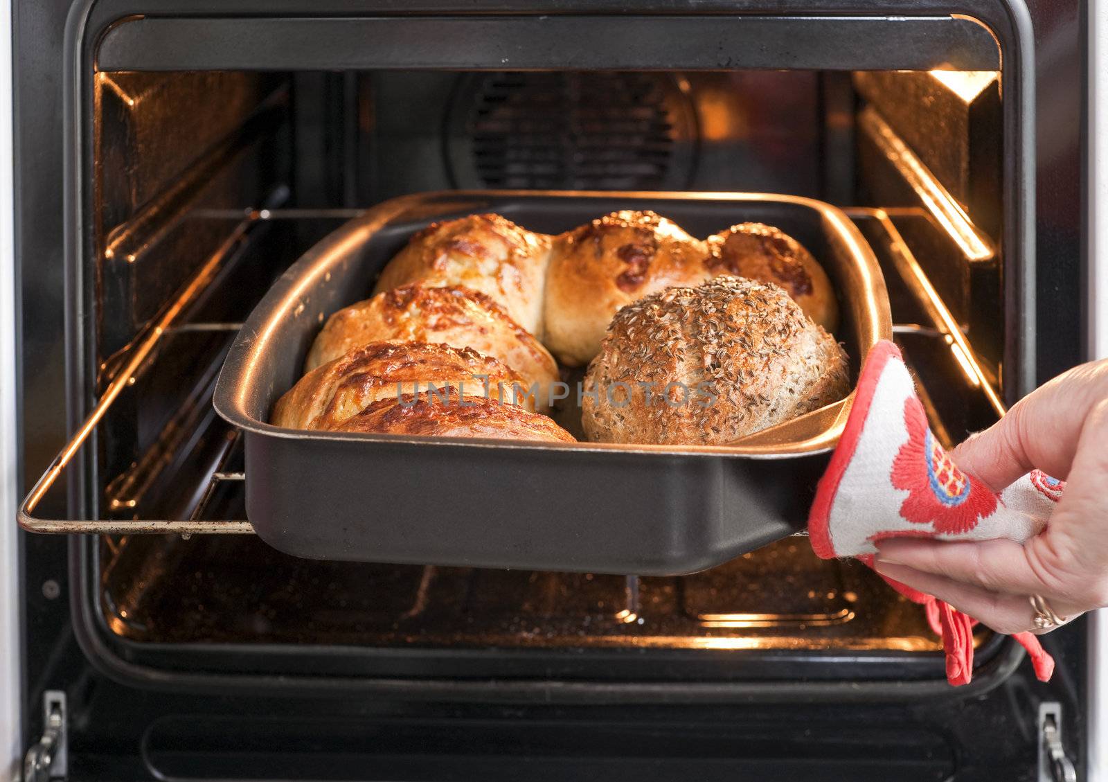 Baker's hand with potholder next to metal cookie sheet with bread in the oven
