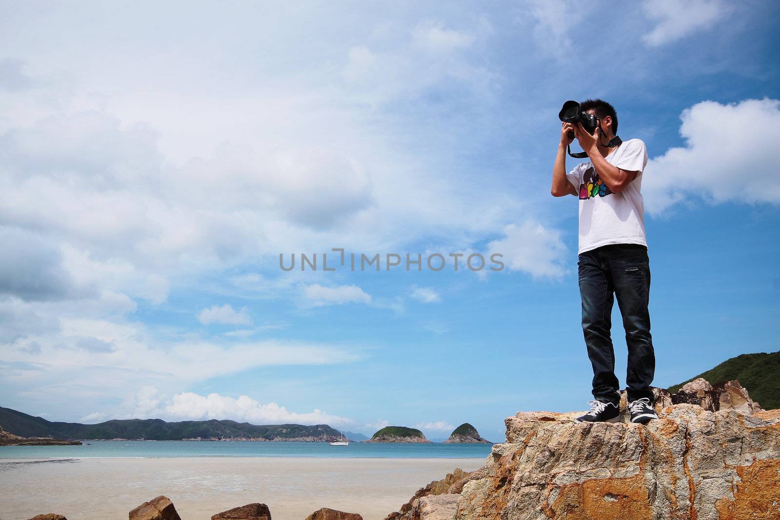 Portrait of a young man standing on a beach with a camera  by cozyta