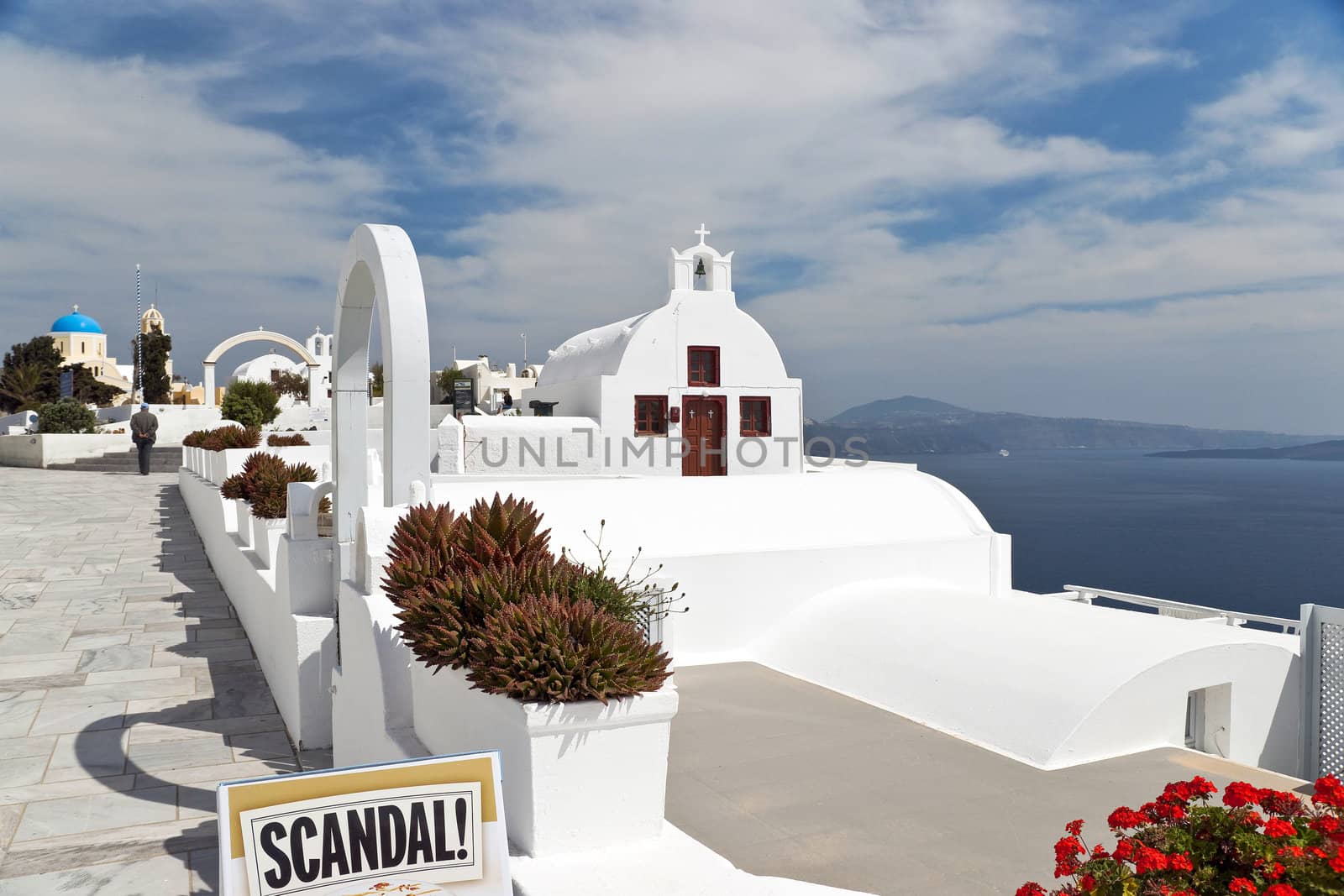 Santorini whitewashed church above Caldera with tablet "Scandal!" in front
