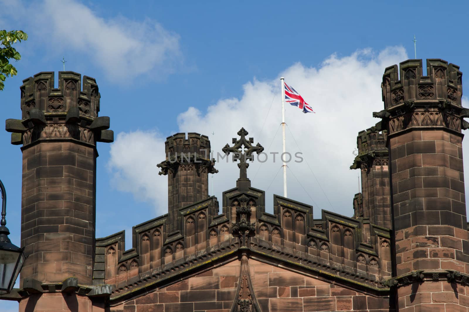 An historic building with towers made from carved ornate red sandstone with a christian cross and a flagpole with a British Union Jack flag.