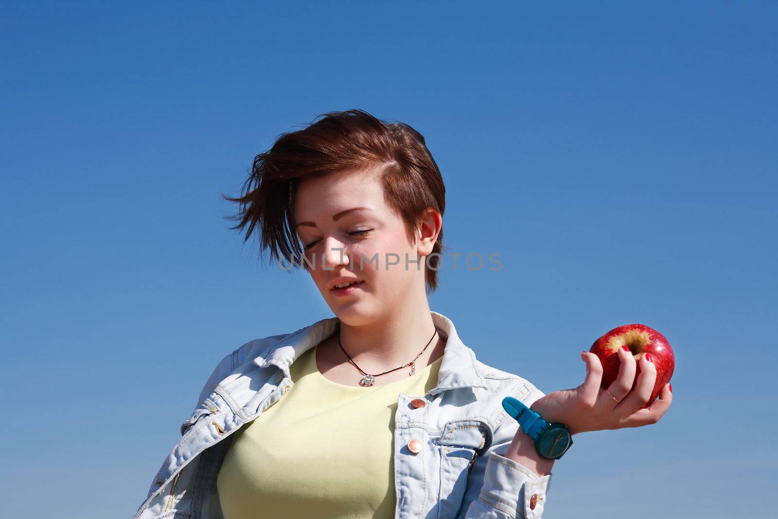 Beautiful young girl handing red apple against blue sky background