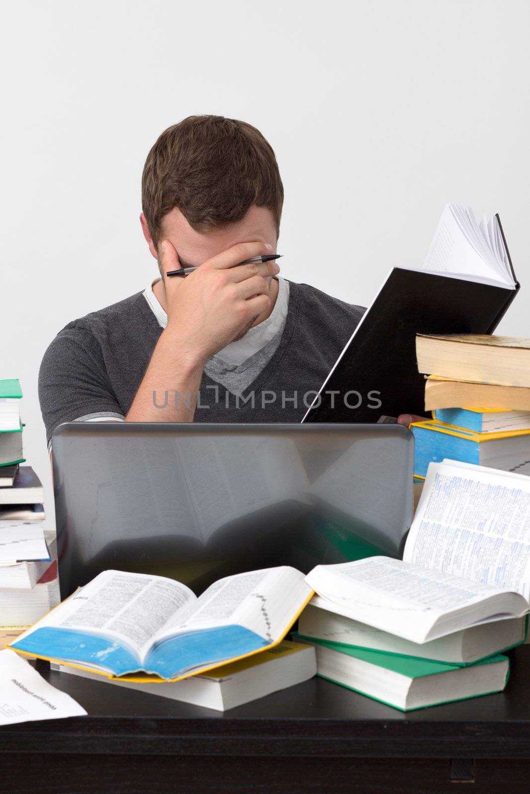 Young Student overwhelmed with studying with piles of books in front of him