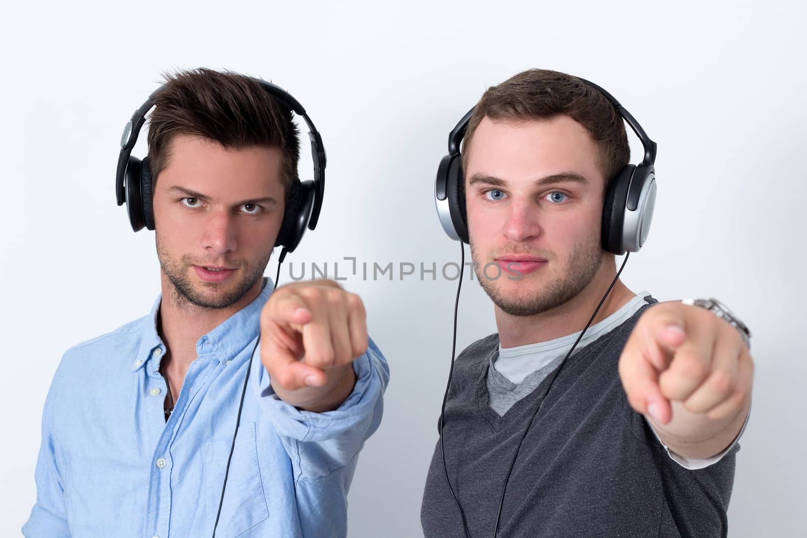 Two friends with headphone listening to music in front of a white background and pointing at camera