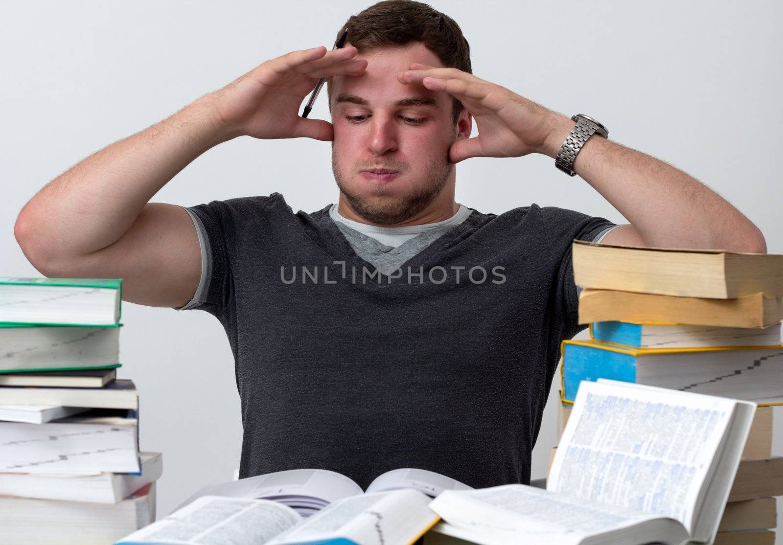 Young Student overwhelmed with studying with piles of books in front of him