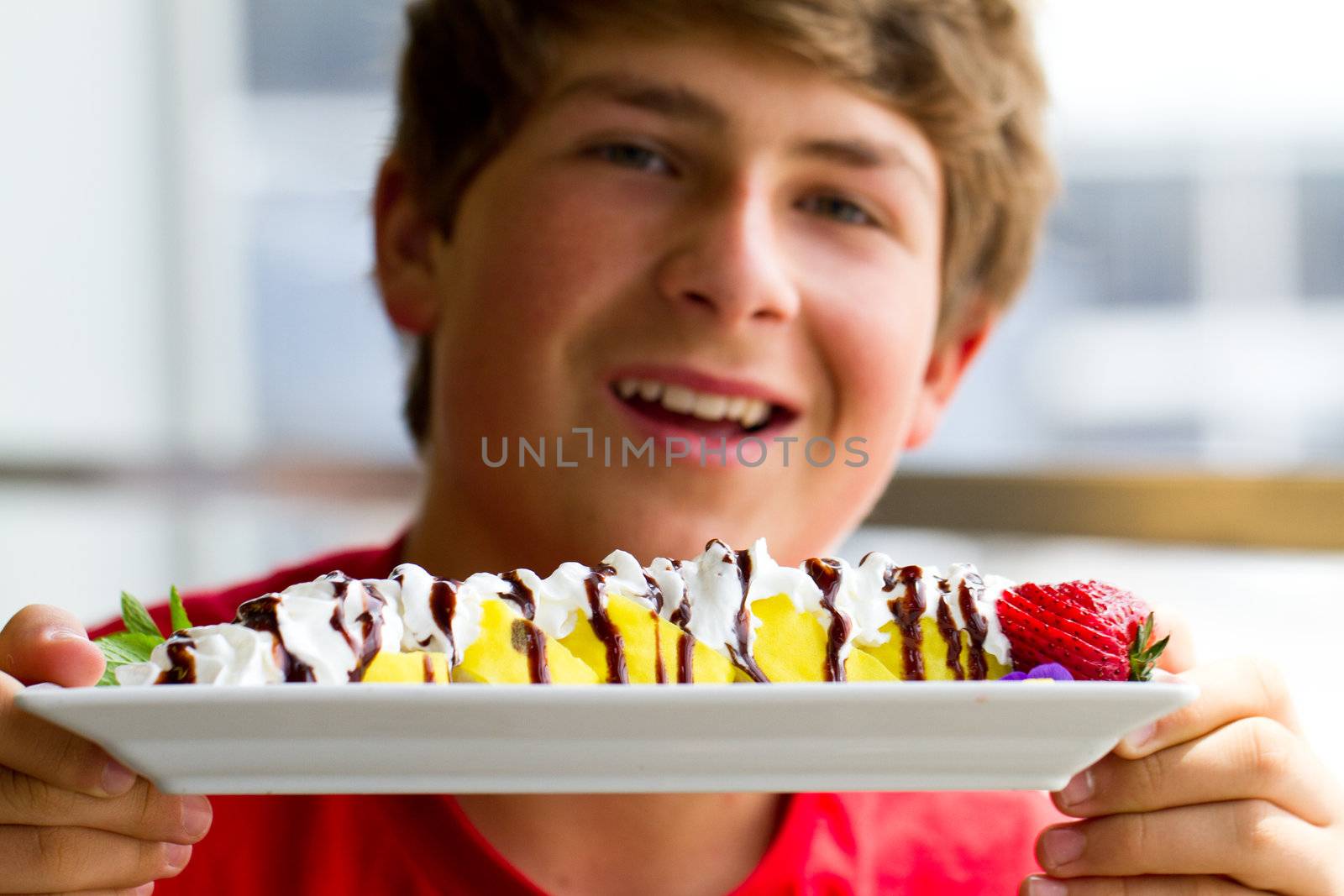 Teenager holding a sushi dessert made with Bannana, strawberries, chocolate and whip cream