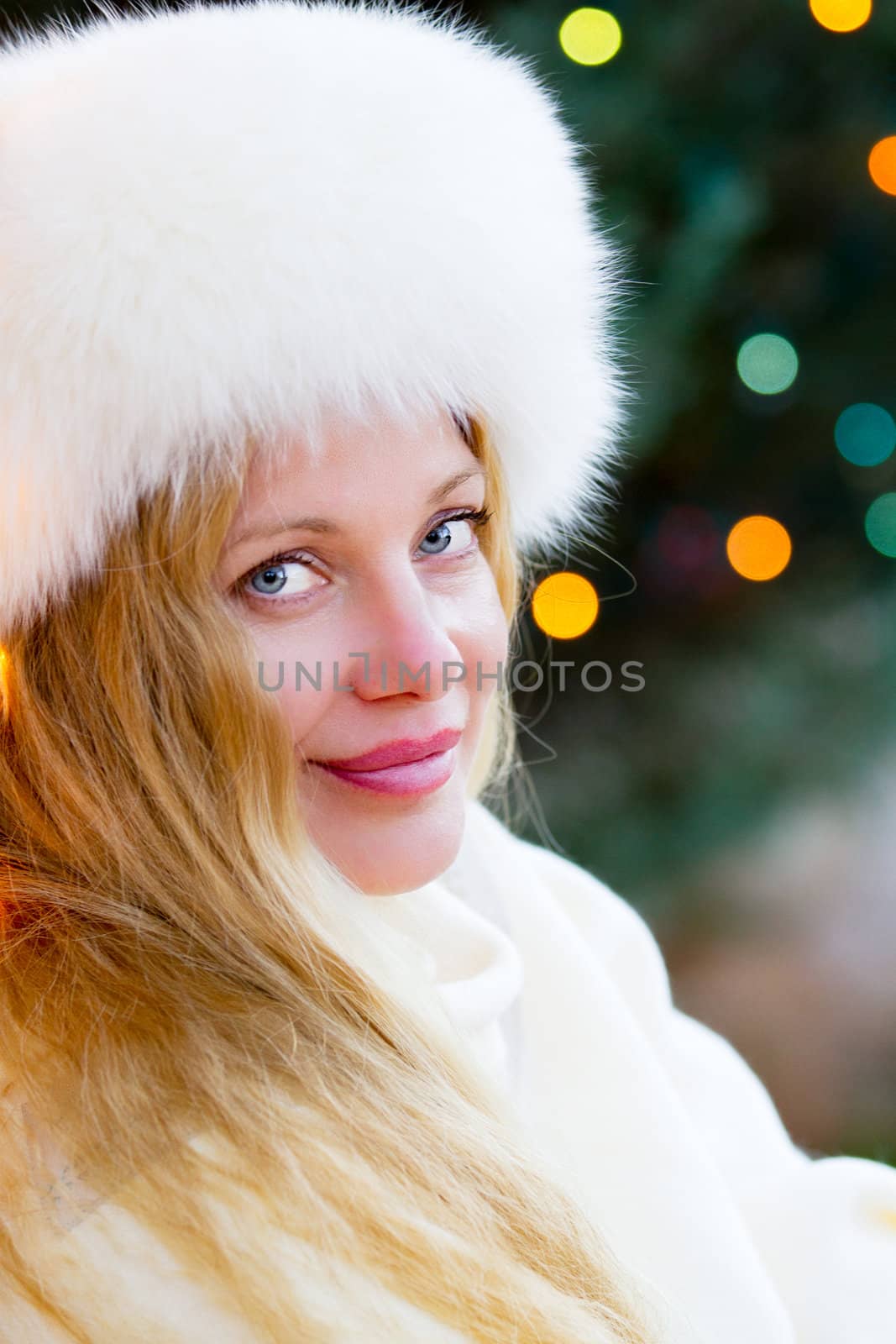 Pretty Blonde Woman wearing a White Fur Hat with Christmas Lights behind her