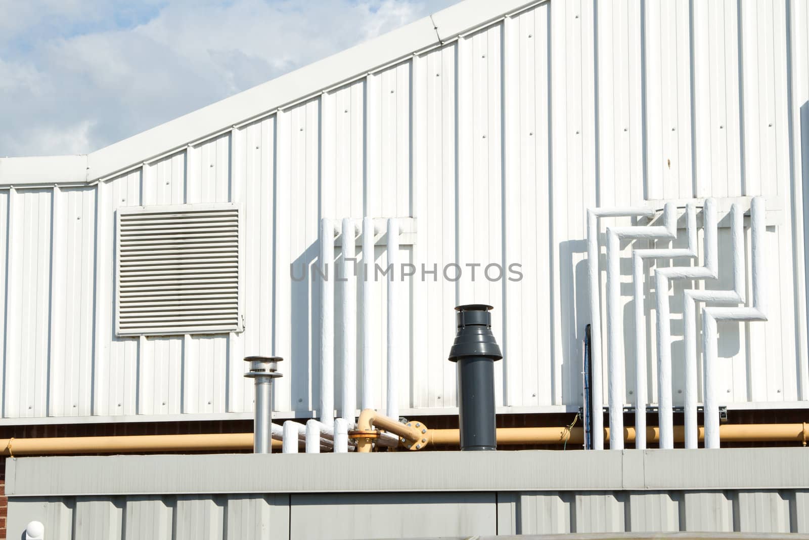 A section of an industrial unit with vent panel and a variety of piping.