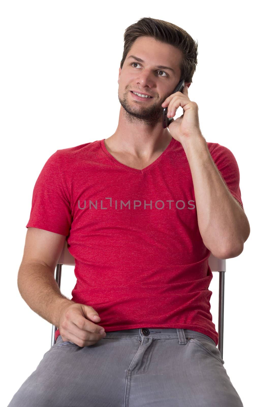 Brunette male student in red t-shirt talking on a cellphone while sitting on a chair