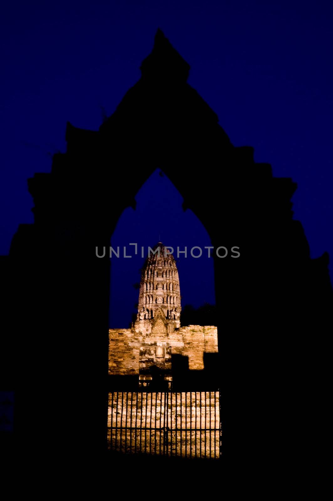 Iluminated Stupa under a dark blue night sky view through a stone gate in Ayutthaya. Ayutthaya city is the capital of Ayutthaya province in Thailand. Its historical park is a UNESCO world heritage.