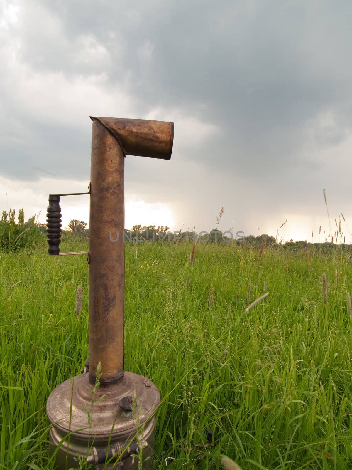 Russian teapot (samovar) in green field under rainy sky