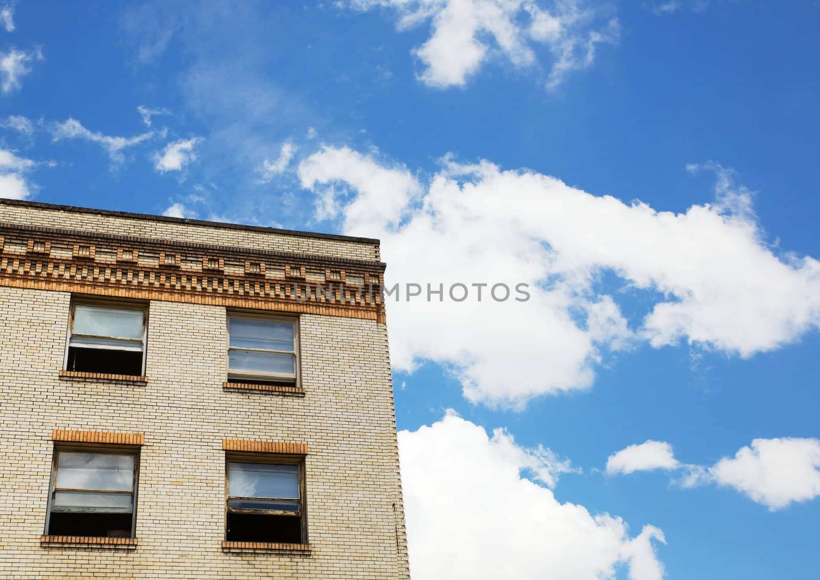 Old Tan brick building with four window against a brilliant blue sky with puffy white clouds