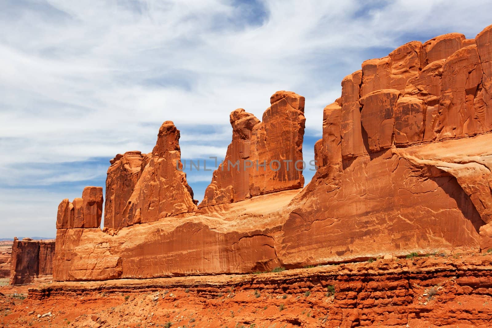 Right side of National Park Avenue with high redstone walls along diagonal with blue wispy cloud sky