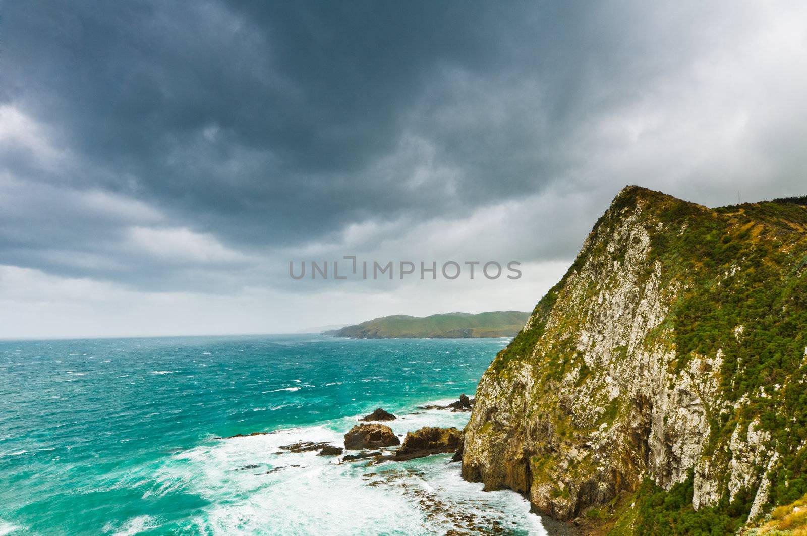 Cliffs under thunder clouds right before a storm and turquoise ocean