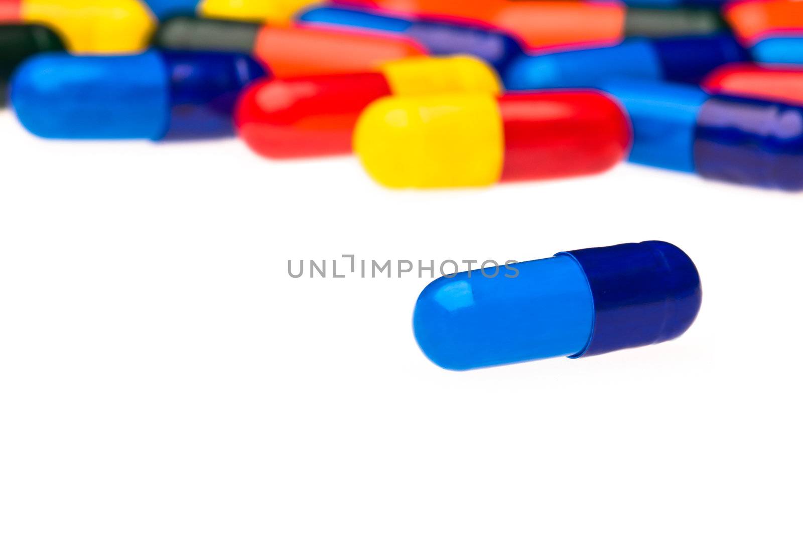 One blue capsule in front of many colorful, blurry in the background
