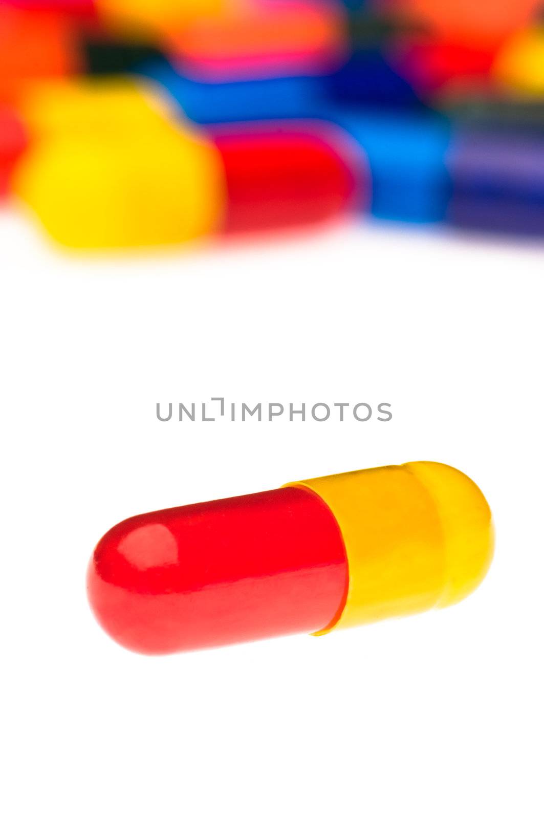 One red yellow capsule in front of many colorful, blurry in the background