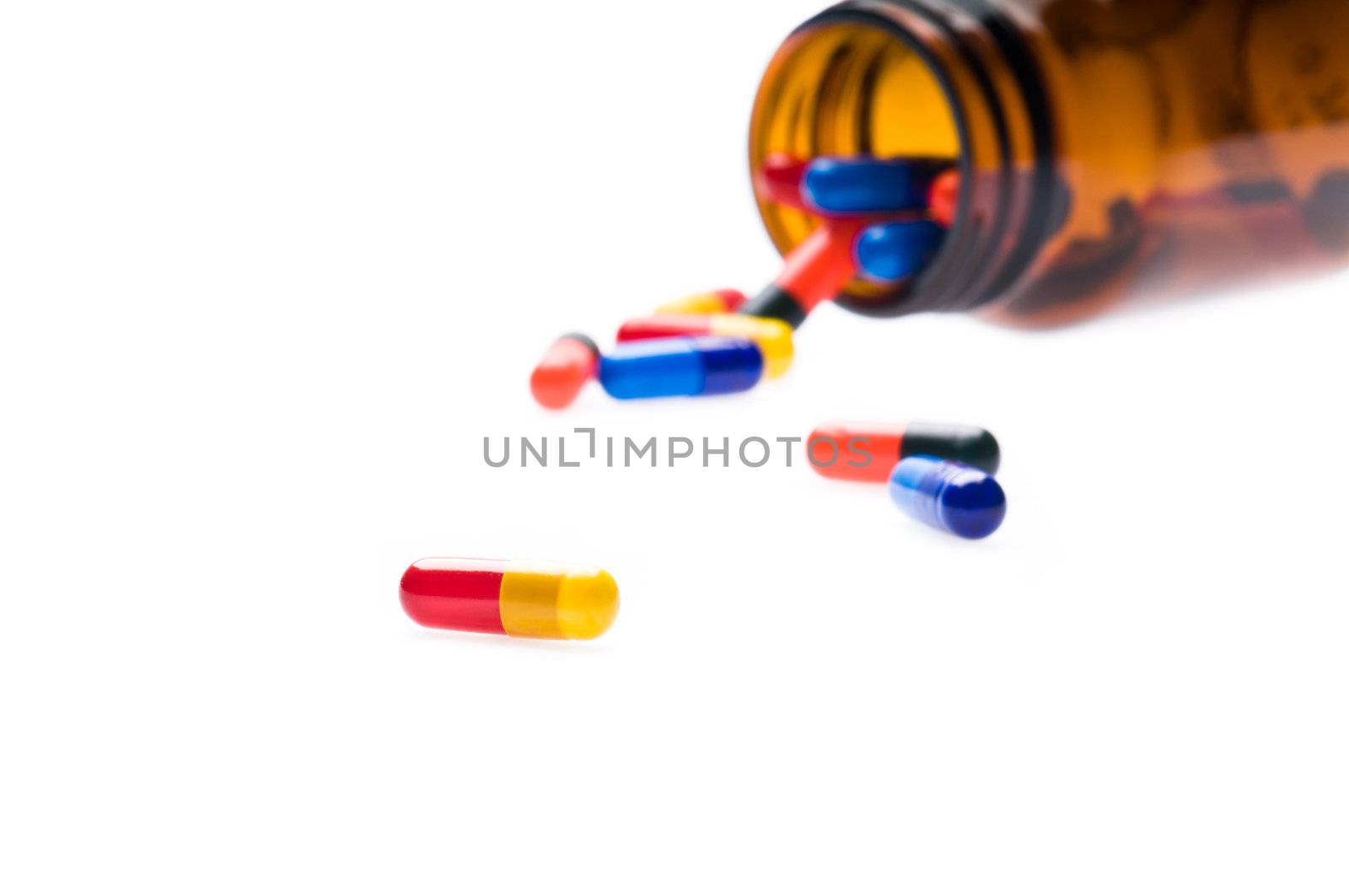 Open pharmaceutical bottle which spills colored capsules over white