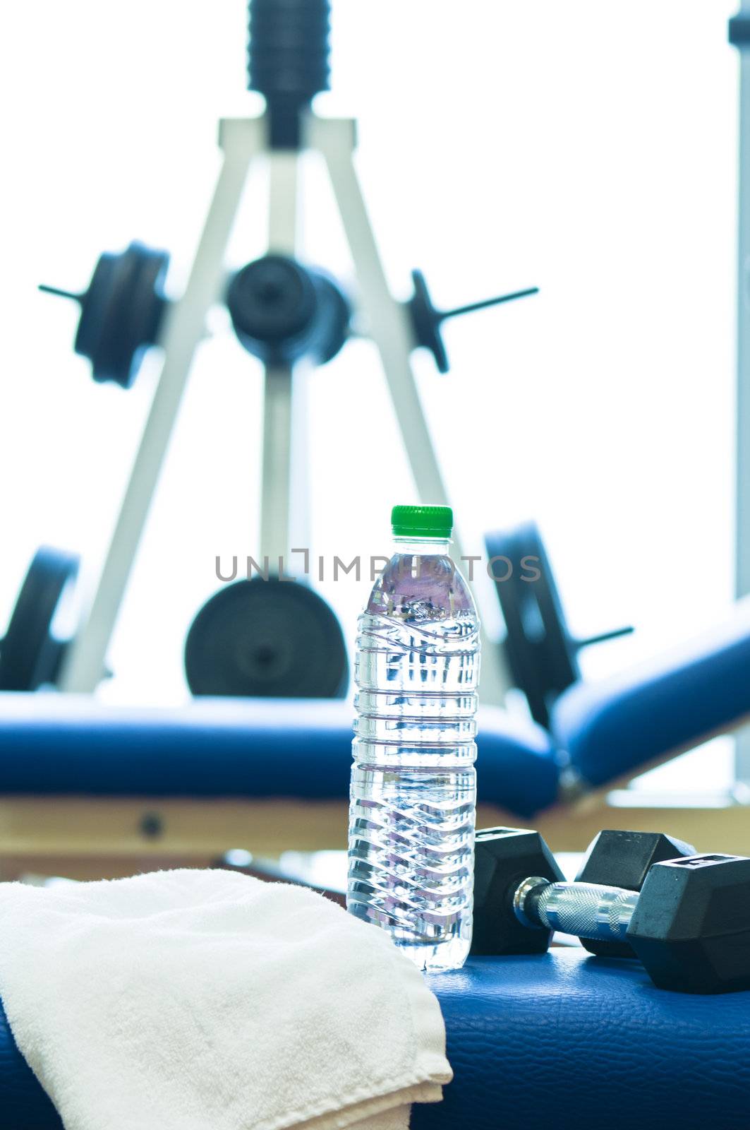 Weights stand, bench of a gym with towel and water bottle blurry background