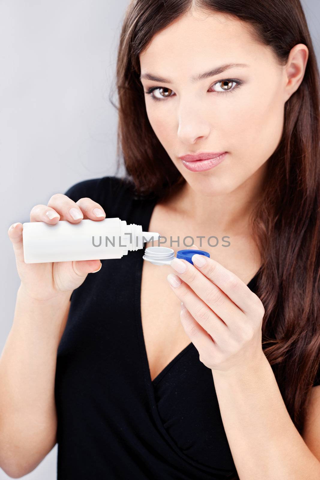 Young woman holding contact lenses cases and bottle of cleaning liquid, focus on bottle