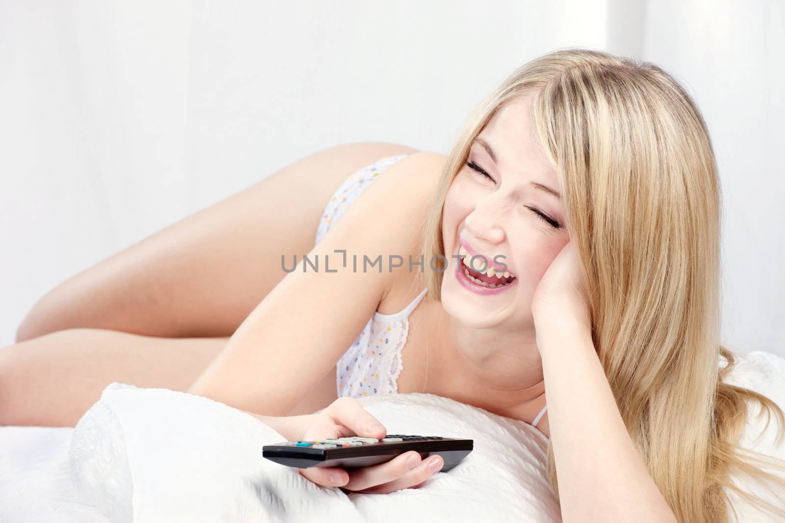 Woman laughing in bed and holding remote controller