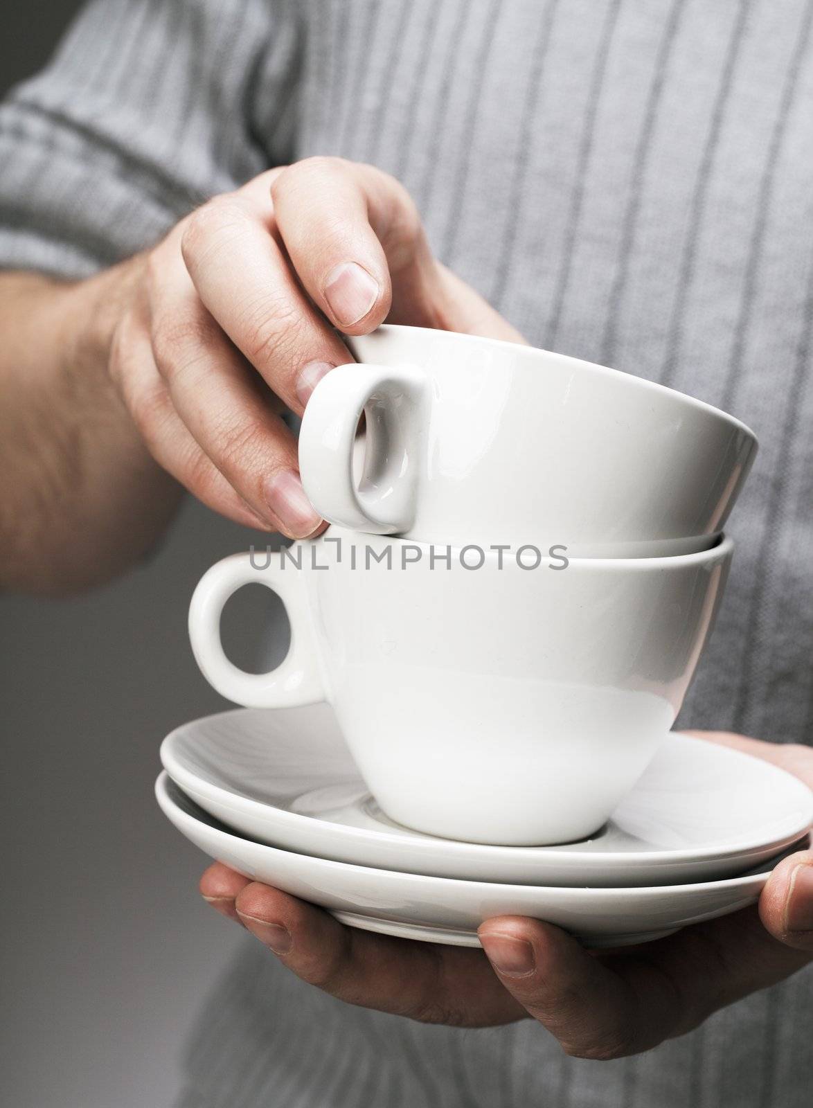 Man holding white porcelain coffee cups in his hands.