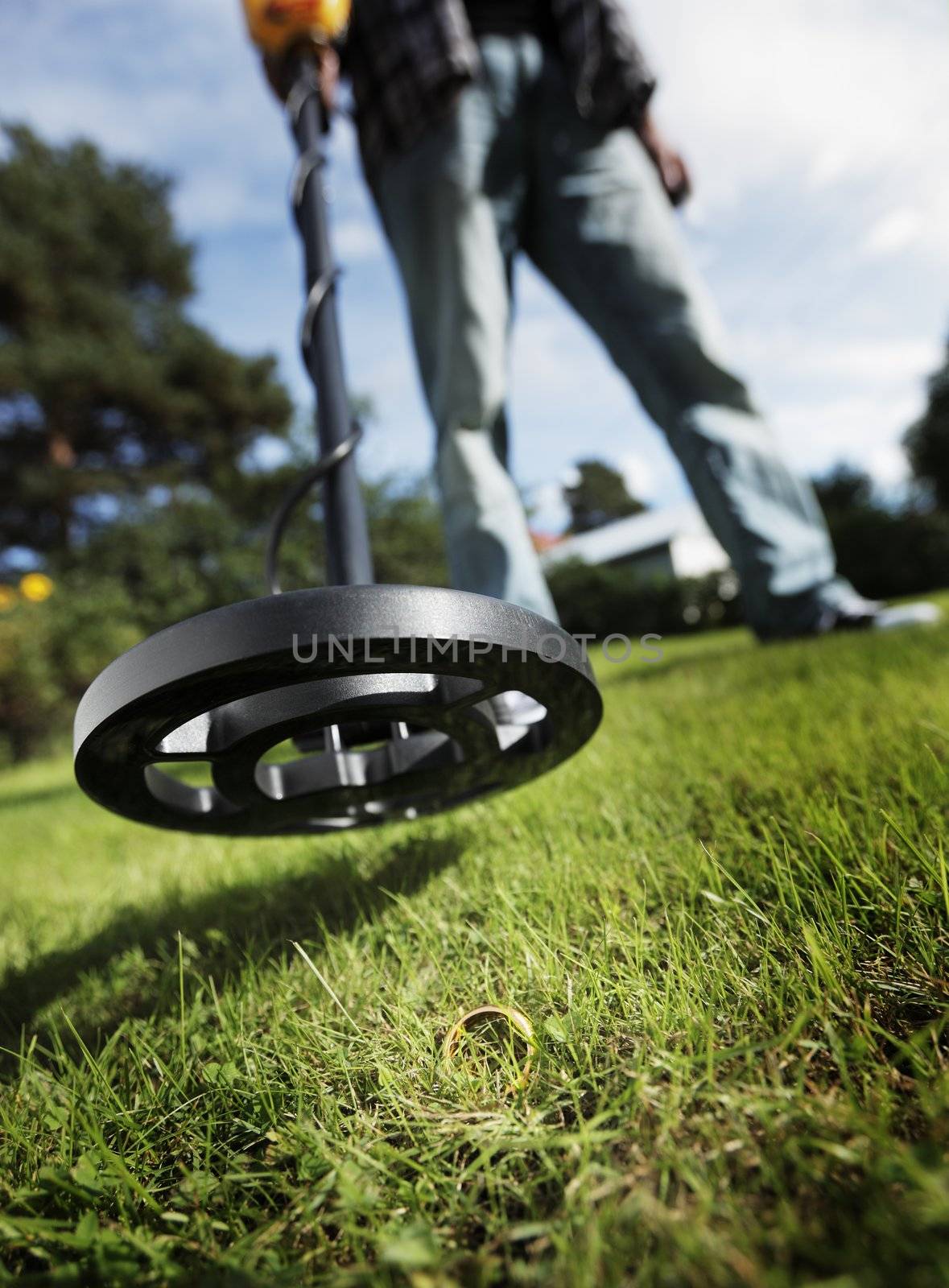 Man finding a gold ring in grass using a metal detector.